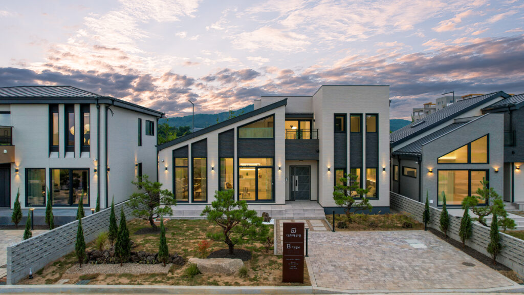 Exterior wide shot of a collection of high-end homes with ample gardens, slanted roofs, tall windows and plenty of wooden accents.