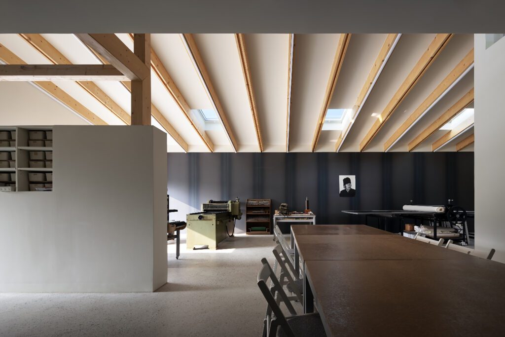 Interior view of a studio with large desks and workstations. The ceiling has thin wood strips with skylights in between them.